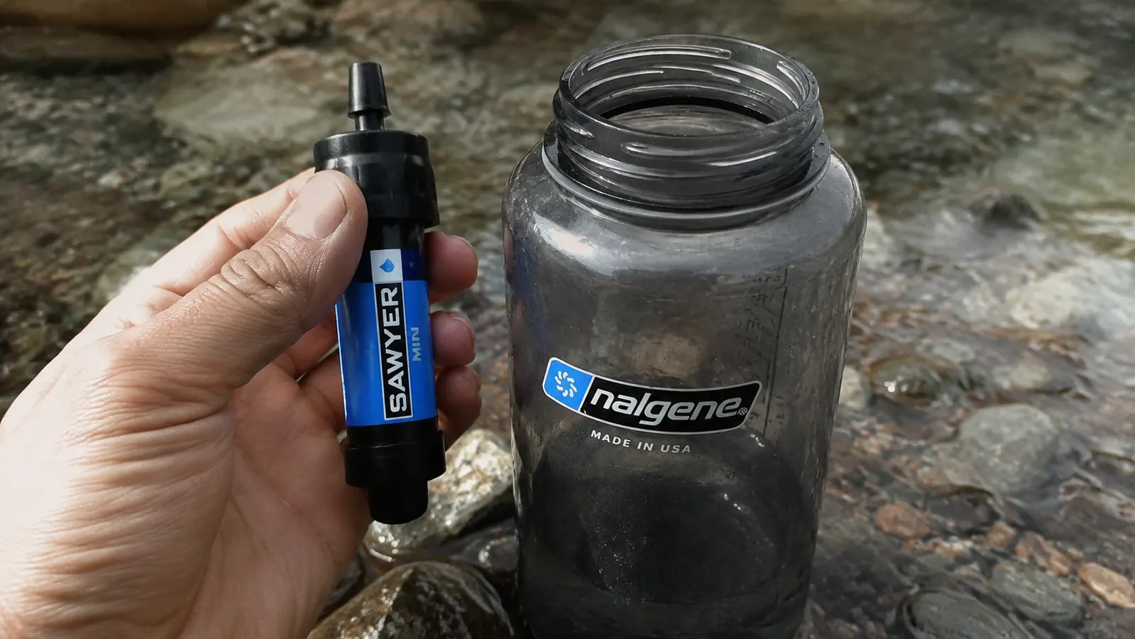 Hand holding a Sawyer Mini filter next to a standard water bottle showing the small size