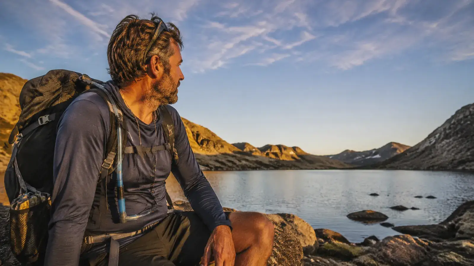Backpacker sitting beside a lake with a Sawyer Mini attached to a hydration reservoir tube