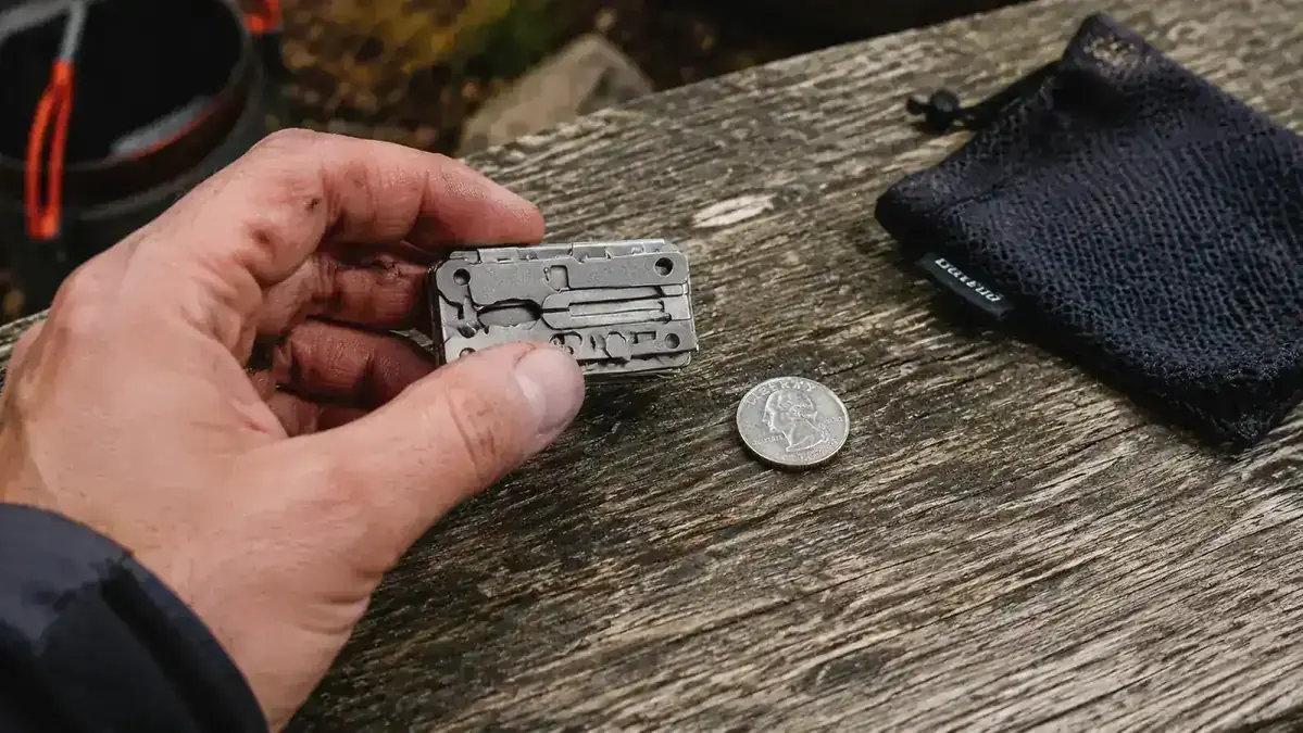 Hand holding a BRS-3000T ultralight stove next to a quarter coin to show scale
