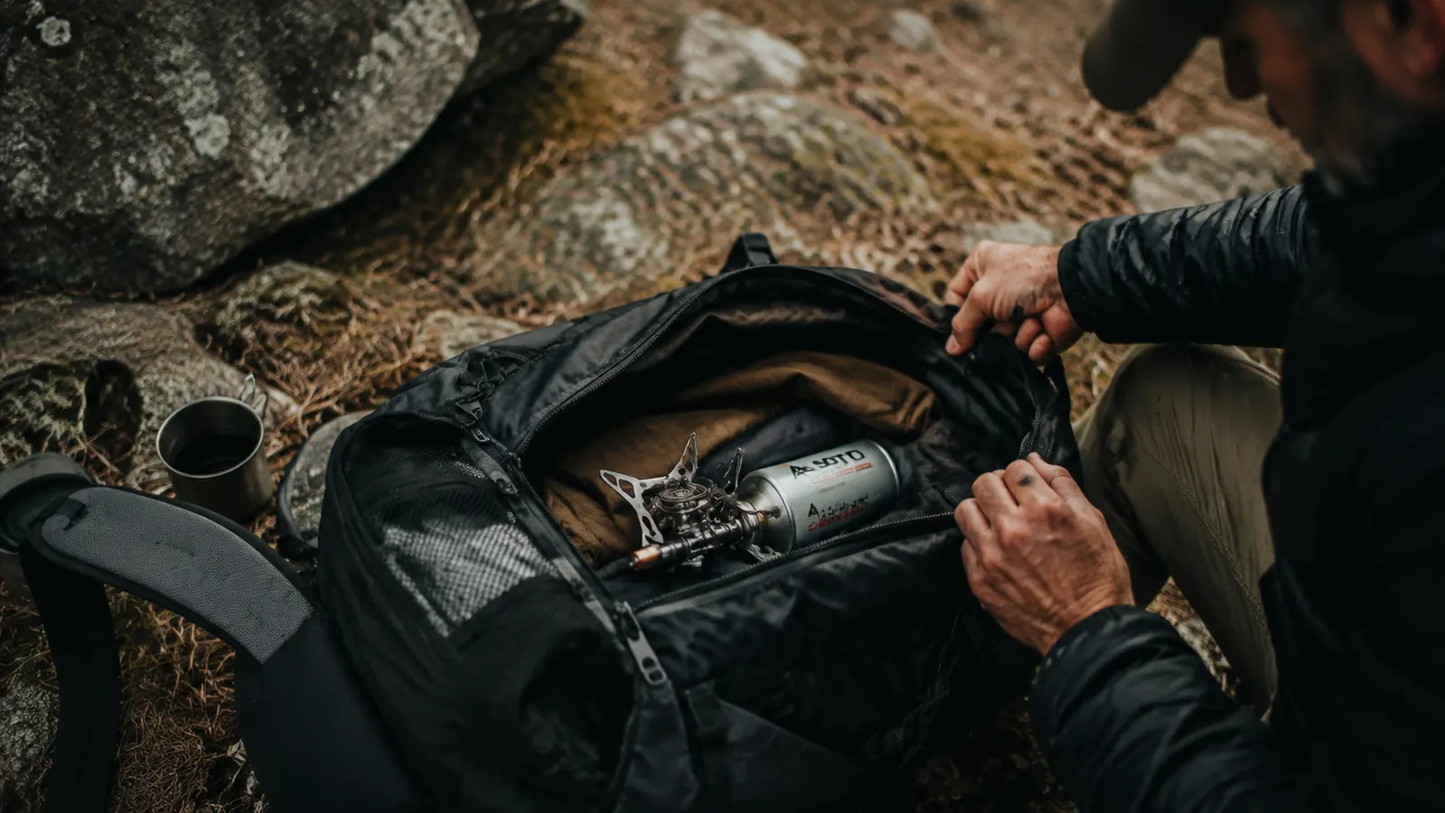 Compact titanium stove and fuel canister sitting on top of a packed backpack