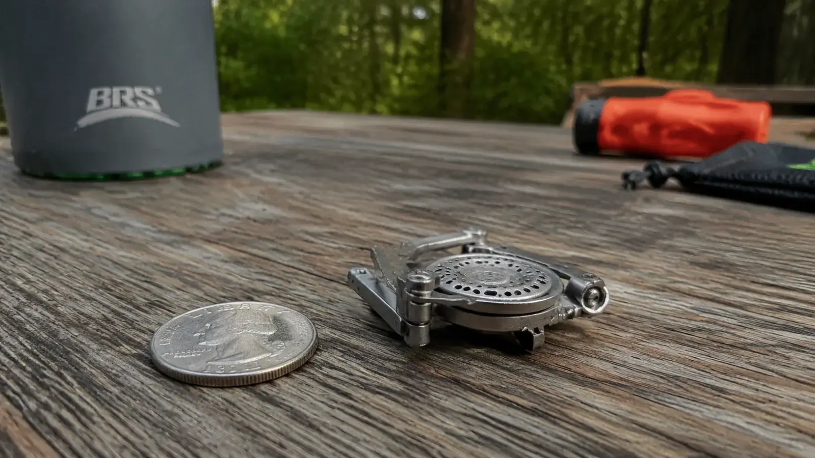 Close-up of BRS-3000T burner head folded flat next to a coin showing its compact size