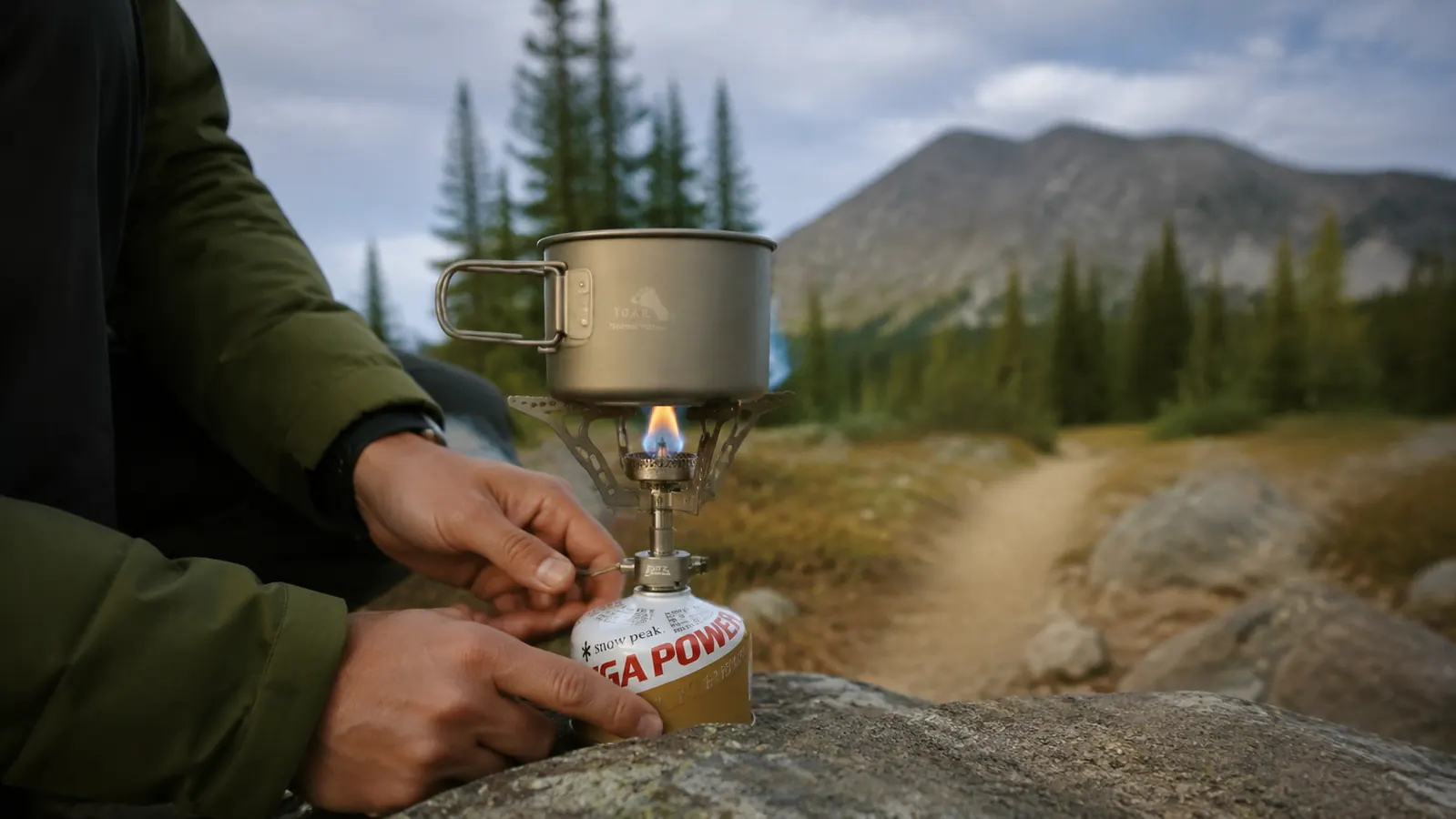 BRS-3000T stove attached to a 100g fuel canister with a titanium pot on top, hands adjusting the flame
