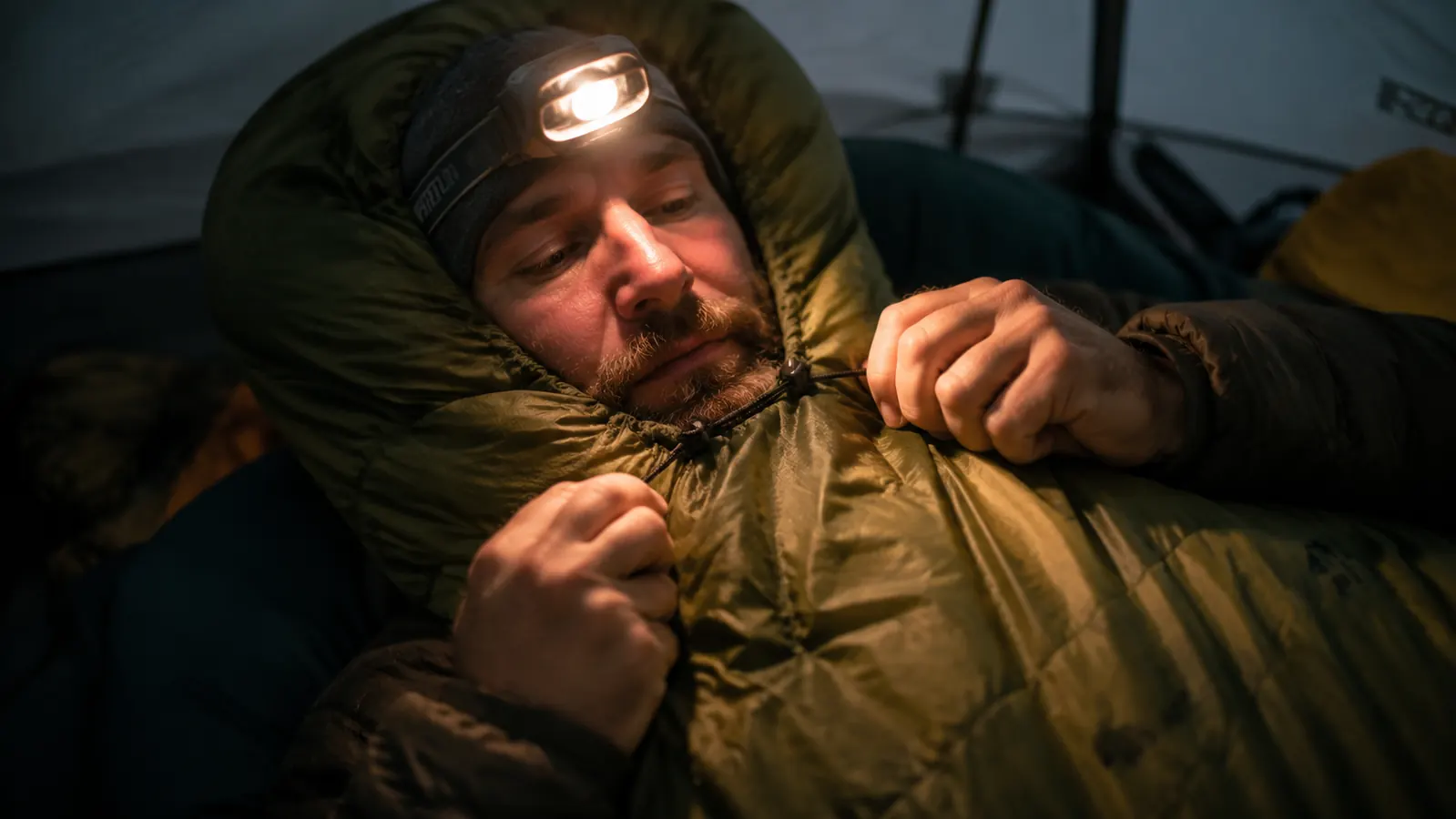 Hands cinching the mummy hood drawstring of the Teton Sports Celsius bag inside a tent