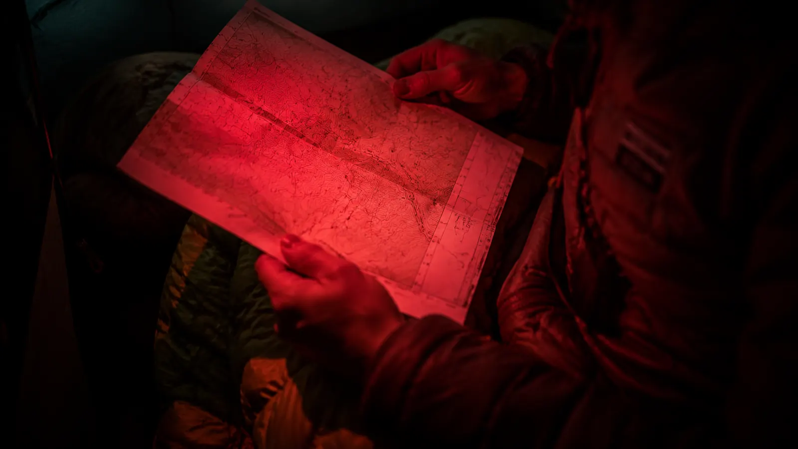 Camper reading a map inside a tent by red headlamp light at night