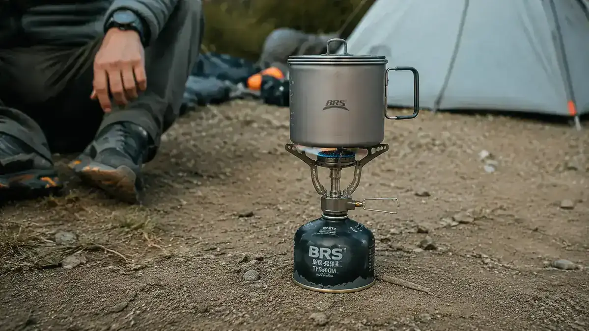 BRS-3000T ultralight titanium stove screwed onto an isobutane canister, pot balanced on top, campfire ring nearby