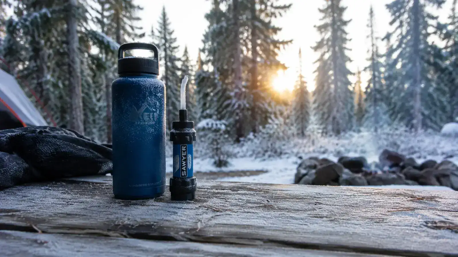 Sawyer Mini filter alongside a frozen water bottle on a winter campsite table