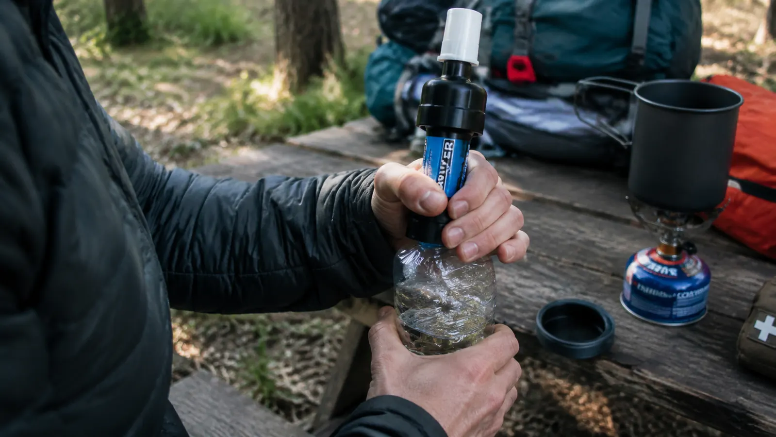 Sawyer Mini attached to a Smartwater bottle being squeezed to filter water at a campsite