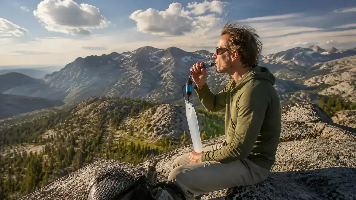 Backpacker drinking from a soft flask with a filter attached while sitting on a rocky ridgeline