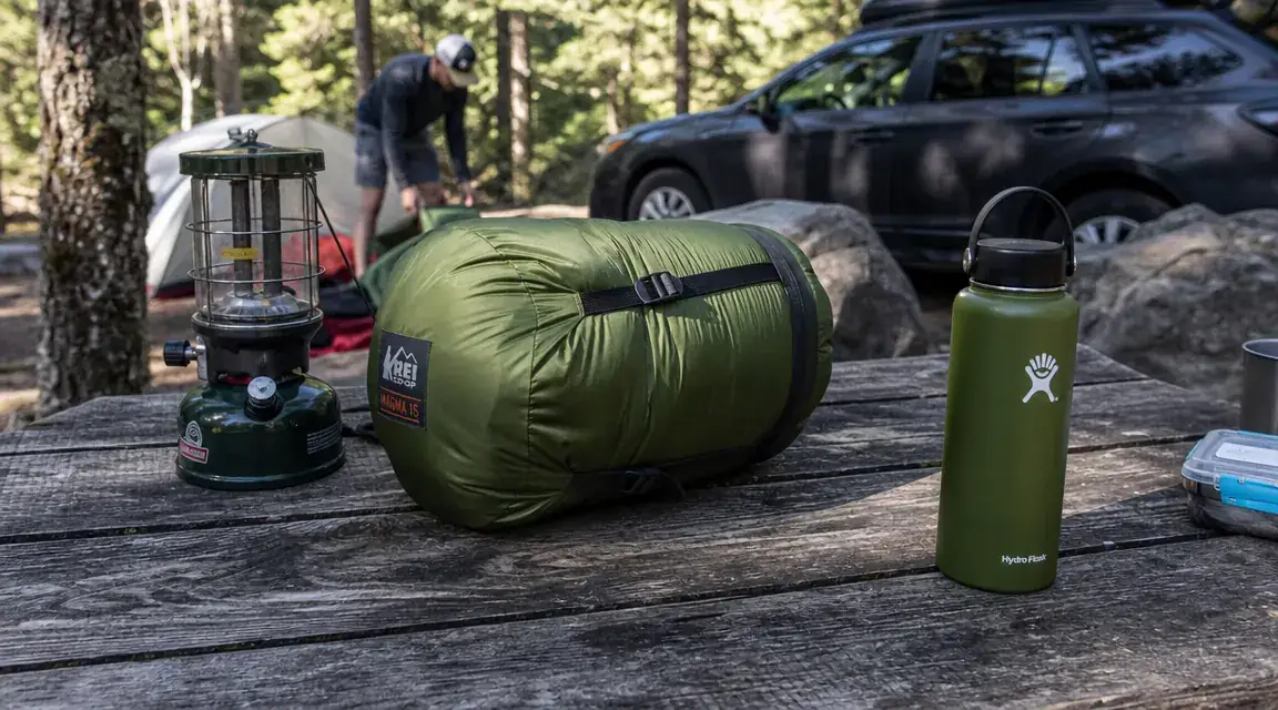 Sleeping bag compressed into its stuff sack next to a camp stove and water bottle for size comparison